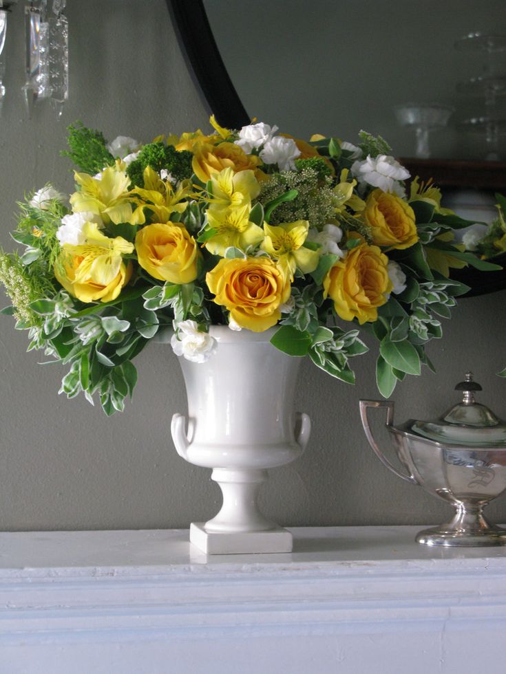 a white vase filled with yellow and white flowers on top of a table next to a mirror