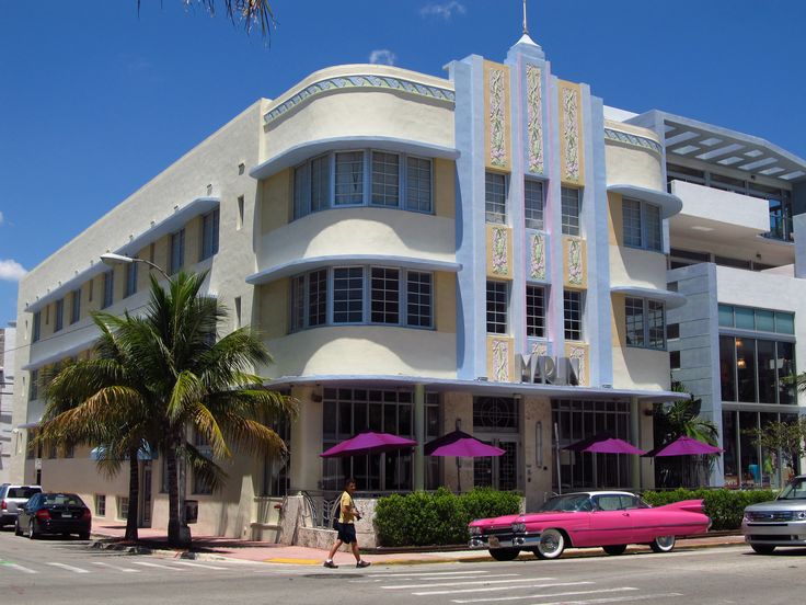 a pink car is parked in front of a white building with purple umbrellas and palm trees