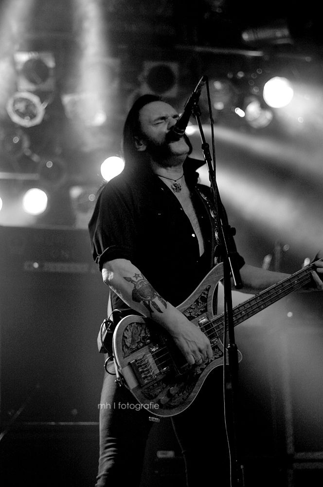 a man with long hair playing guitar in front of microphones and lights on stage