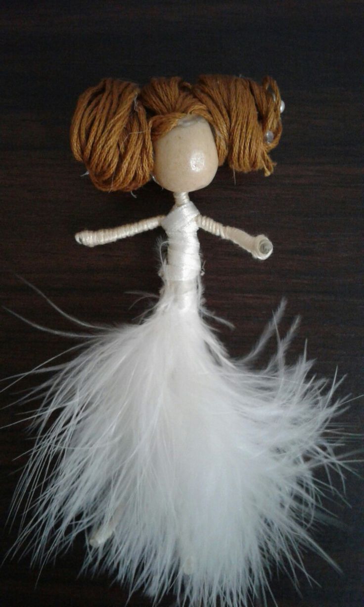 a doll made out of yarn and white feathers on a table with a black background