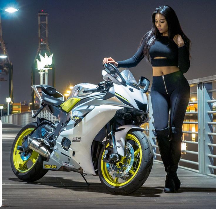 a woman standing next to a white and yellow motorcycle in front of a bridge at night