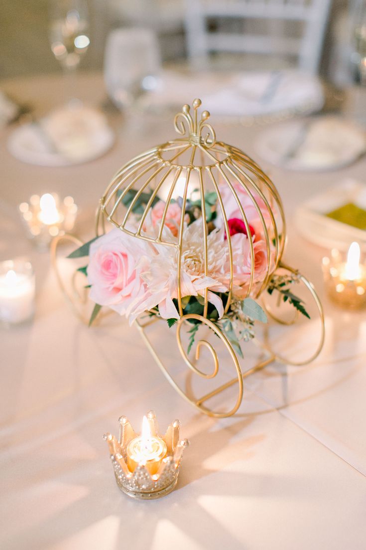 a birdcage filled with flowers sitting on top of a table next to candles