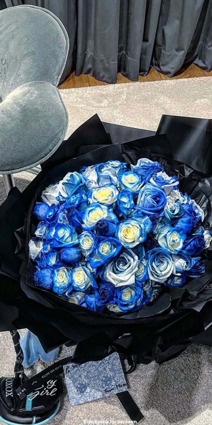 a large bouquet of blue roses sitting on top of a black bag next to a chair