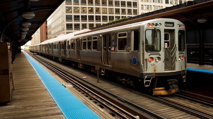 a silver train traveling down tracks next to tall buildings