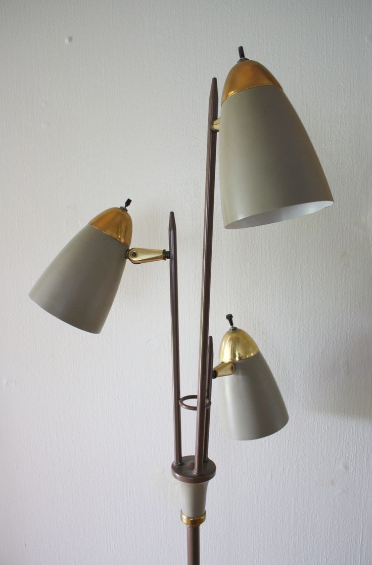 three light floor lamp in the corner of a room with white walls and two lamps on each side