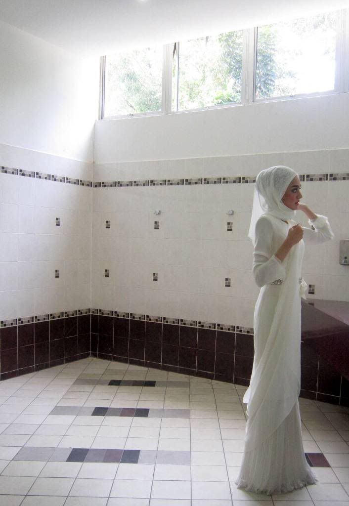 a woman in a white dress is standing in a room with tiled floors and walls