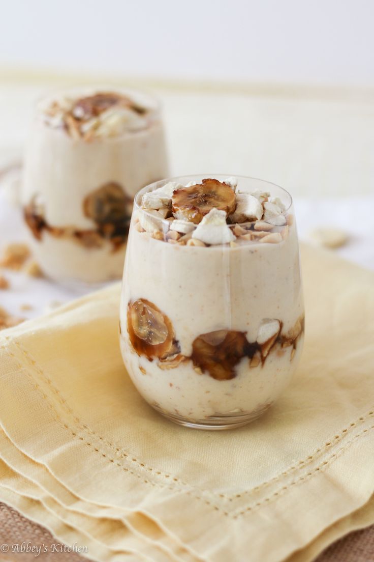 two glasses filled with dessert sitting on top of a table next to napkins and cloth