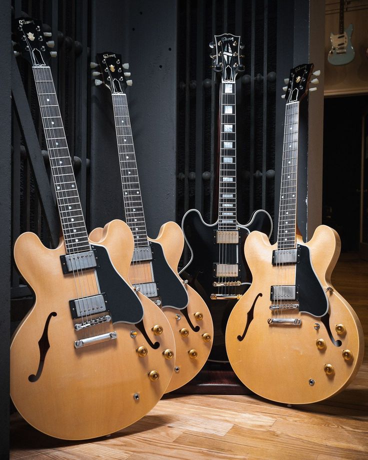 three electric guitars lined up next to each other on a hard wood flooring area