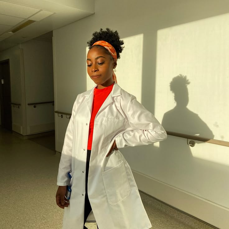 a woman in a white lab coat standing next to a wall