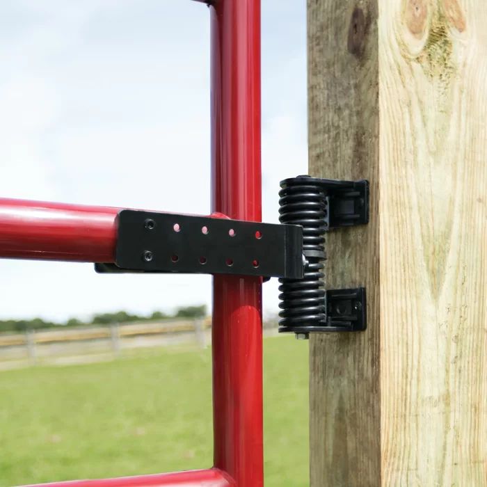 a red gate with two black latches on it and a field in the background