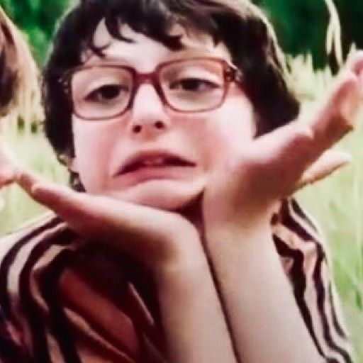 a young boy wearing glasses sitting in the grass with his hands on his face and looking up