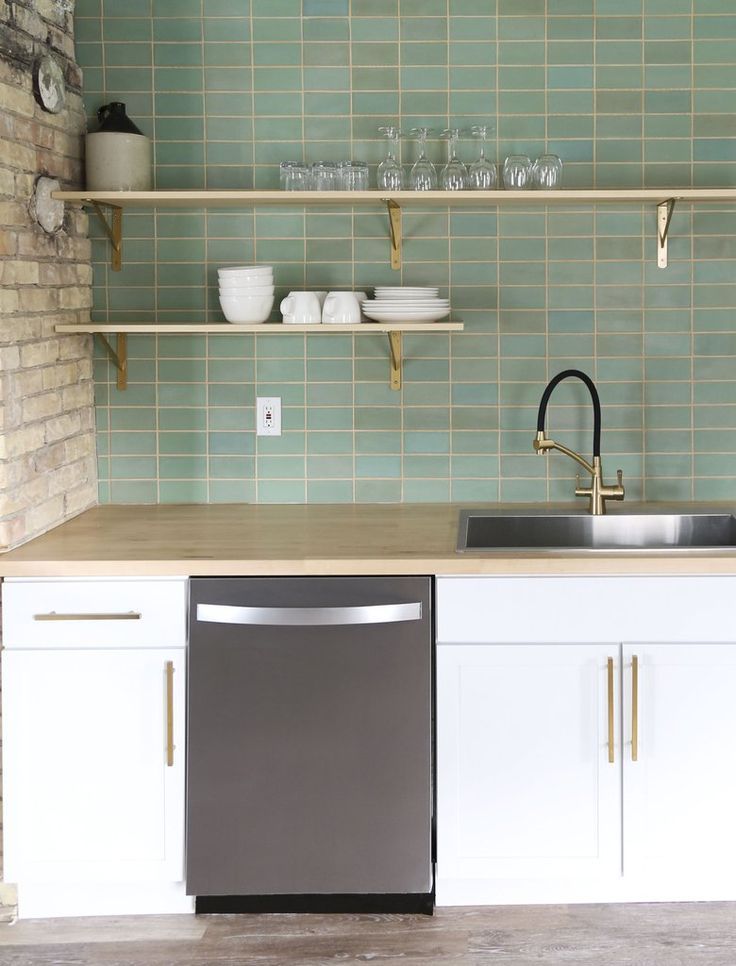 a kitchen with green tile walls and white cupboards, stainless steel dishwasher