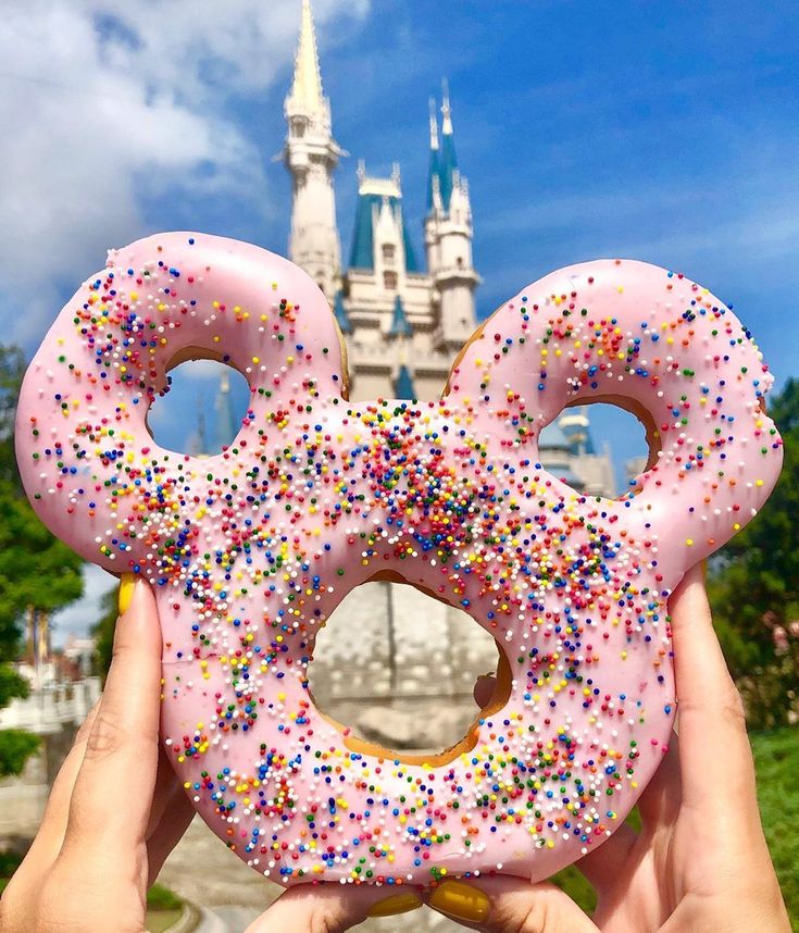 someone holding up a pink doughnut with sprinkles in front of a castle