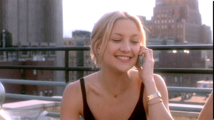 a woman talking on a cell phone while sitting at a table in front of a cityscape