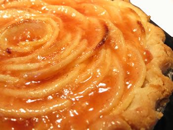 an apple pie with caramel sauce on top sitting on a black plate, ready to be eaten