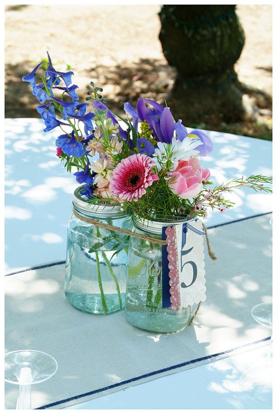 two mason jars filled with flowers sitting on top of a white tablecloth covered table