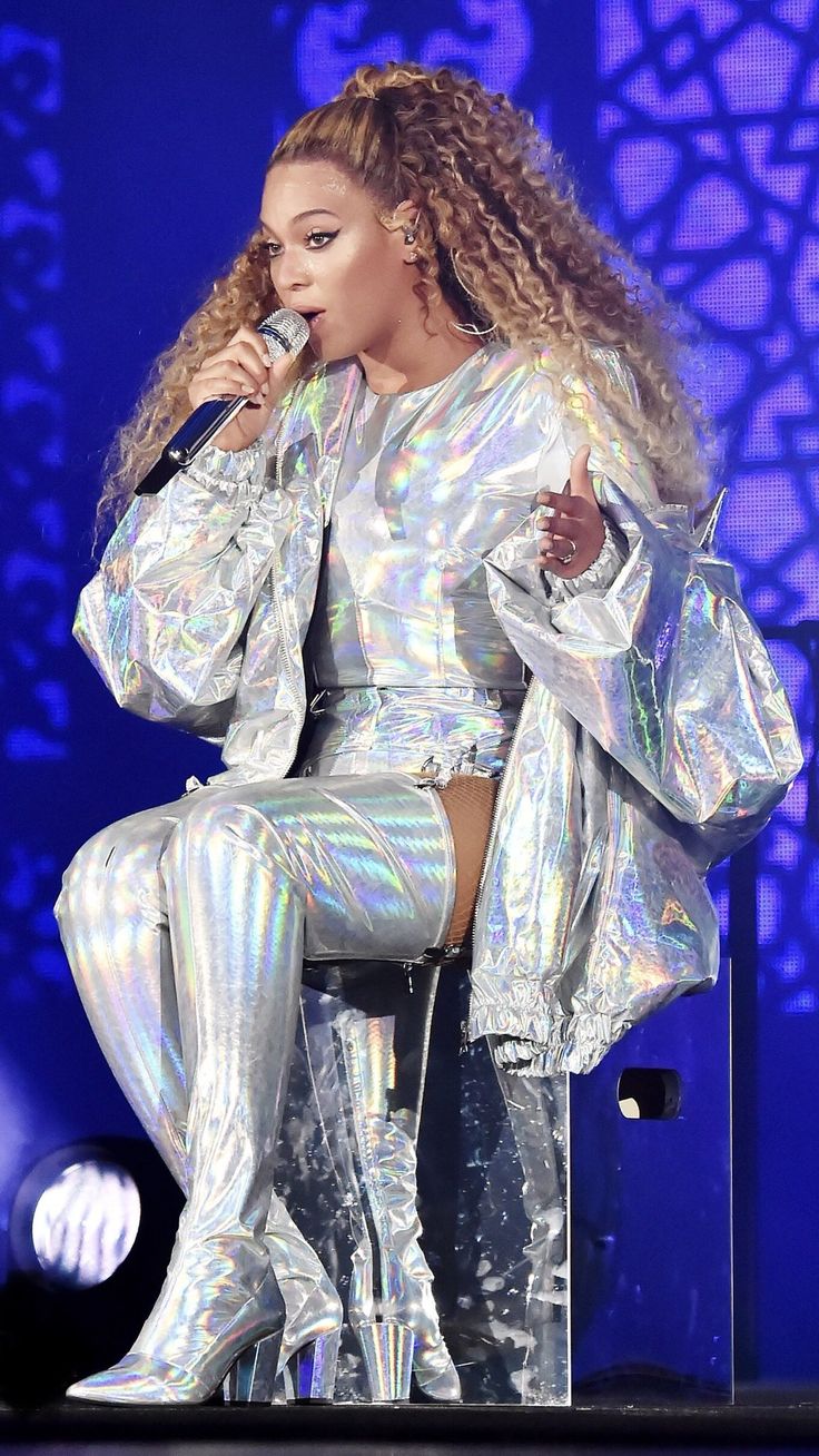 a woman in silver outfit on stage holding a microphone and wearing high heeled boots