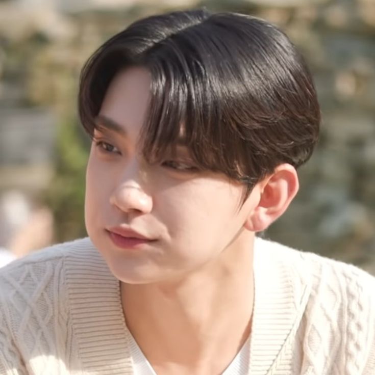 a young man with black hair wearing a white sweater and looking off to the side