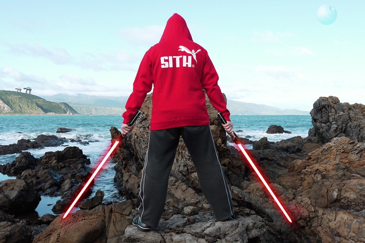 a person in a red hoodie holding two lightsabes on rocks near the ocean