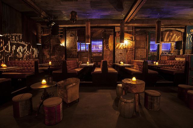 a dimly lit restaurant with wooden tables and stools in the center, lighted by candles