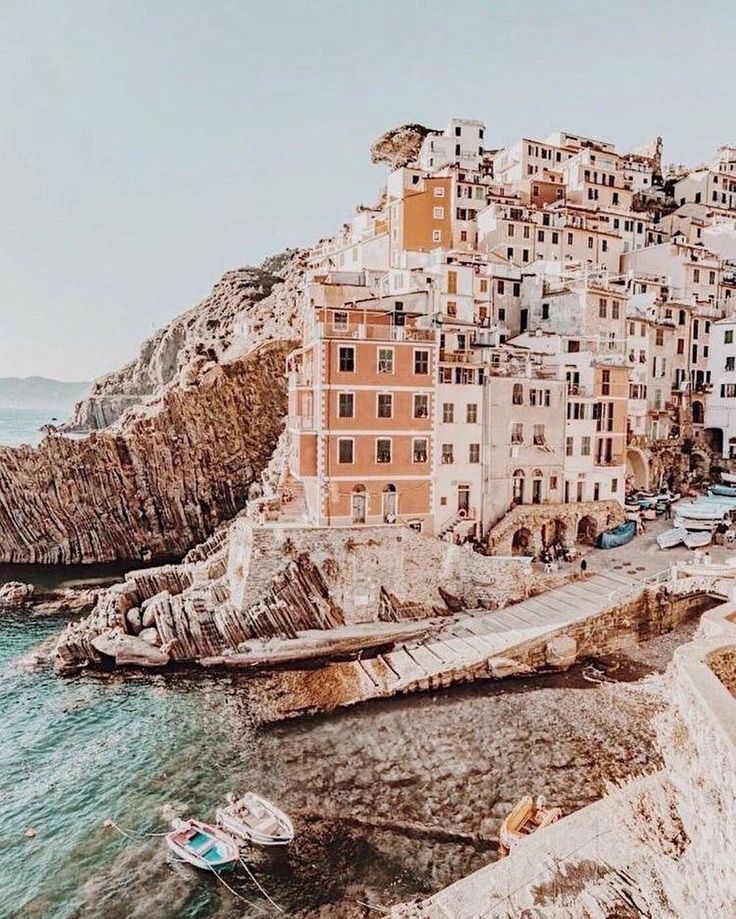 a small boat in the water next to some buildings and cliffs near the ocean with boats parked on the shore