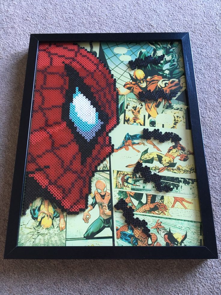 a spiderman cross stitch pattern in a black frame on the floor next to a wall