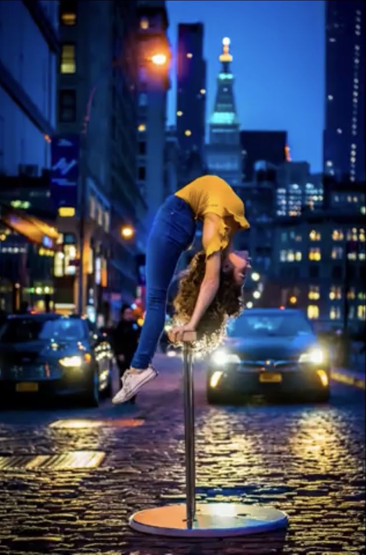 a woman standing on top of a pole in the middle of a city at night