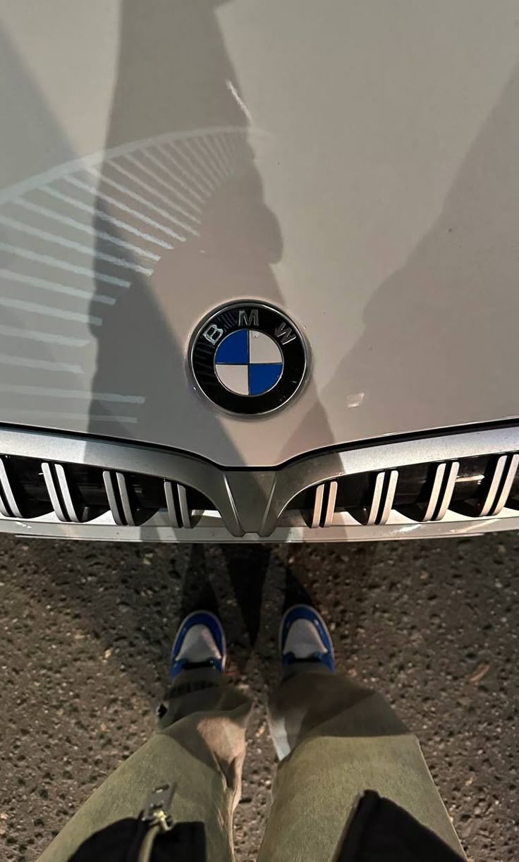 the front end of a bmw car with its emblem on it's grill and two people standing next to it