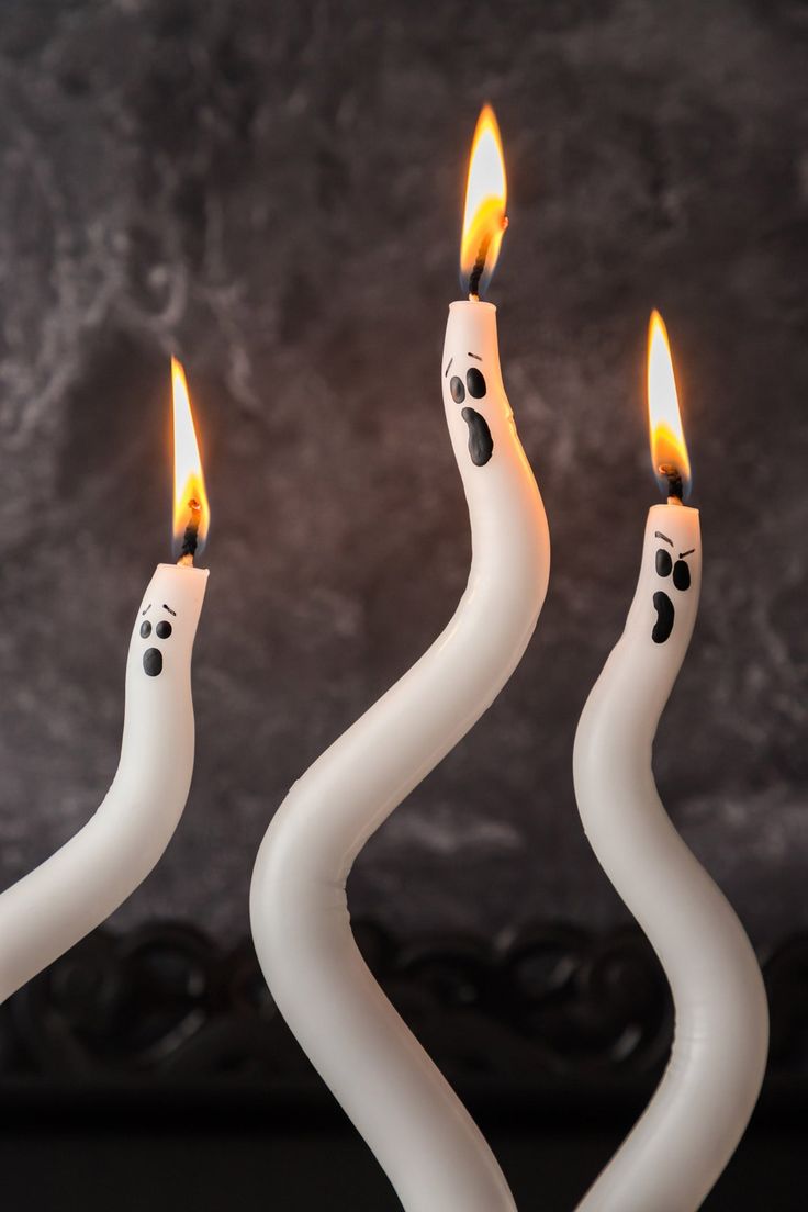 three white candles with faces on them are lined up in the shape of spirals