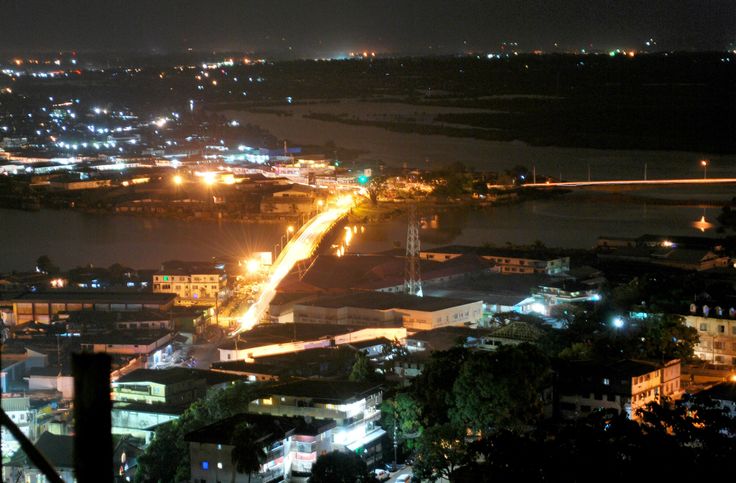 an aerial view of a city at night with lights on the buildings and water in the background