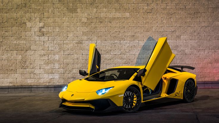 a yellow sports car parked in front of a brick wall with its doors open and lights on