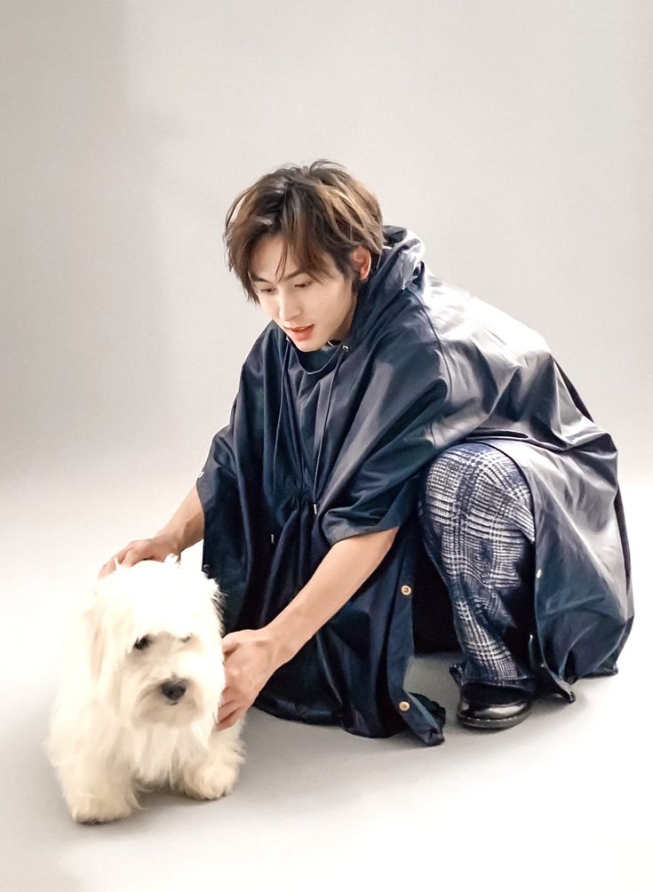 a person kneeling down with a white dog in front of them on a gray background