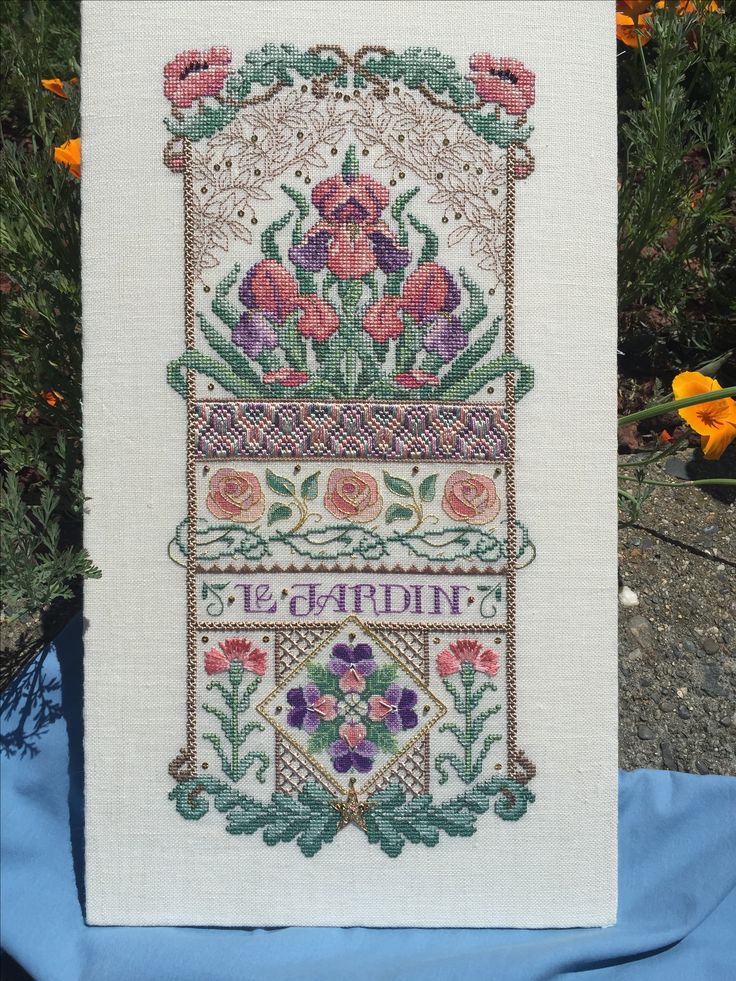 a cross - stitched sign with flowers on it sitting in front of some bushes