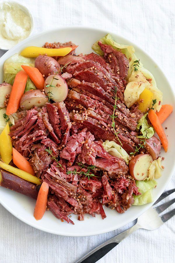 a white plate topped with corned beef and veggies next to carrots