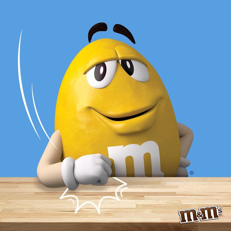 a yellow m & m's egg sitting on top of a wooden table next to a blue background