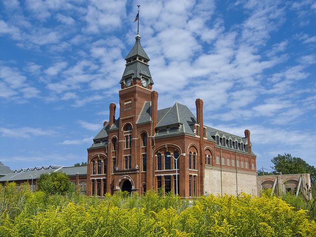 an old brick building with a steeple on top and yellow flowers in the foreground