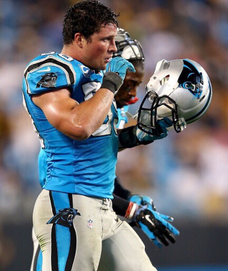 a close up of a football player holding a helmet on his left hand and looking down at the ground