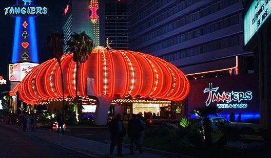 people are walking down the street in front of brightly lit buildings and palm trees at night