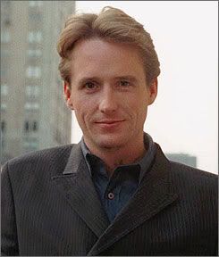 a man wearing a suit and tie standing in front of a tall building with buildings behind him