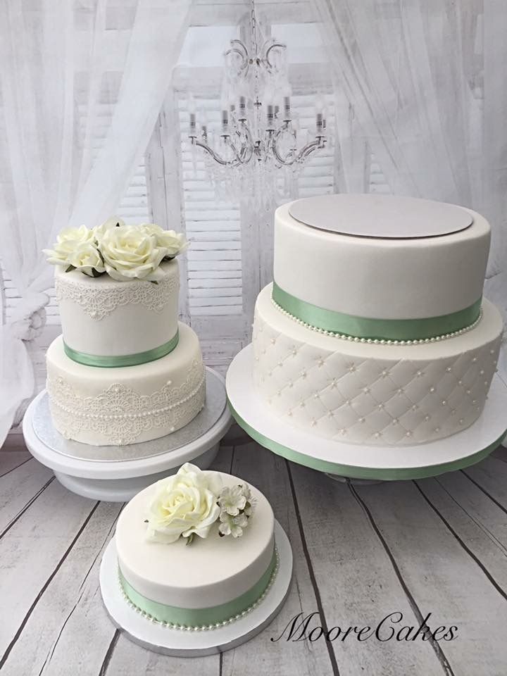 three tiered wedding cakes with white flowers and green ribbon on top, sitting on a wooden table