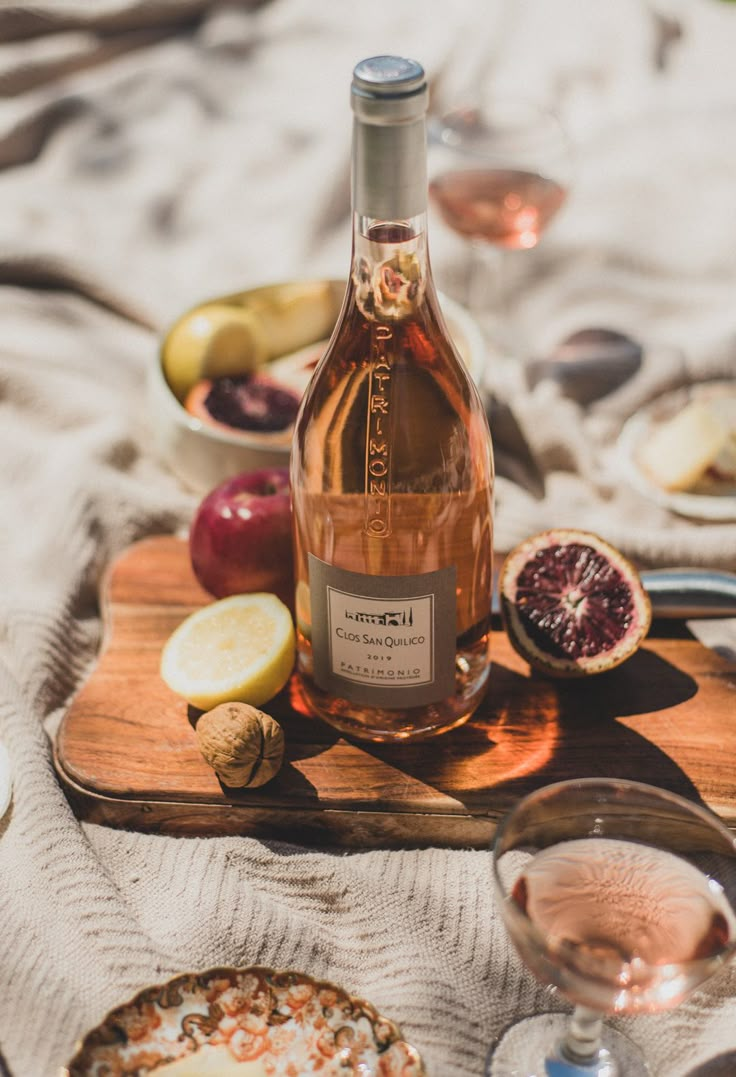 a bottle of wine sitting on top of a wooden cutting board next to some fruit