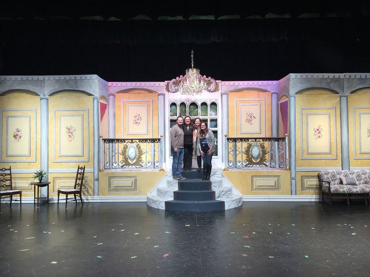 three people standing in front of a stage with yellow and pink painted walls on it