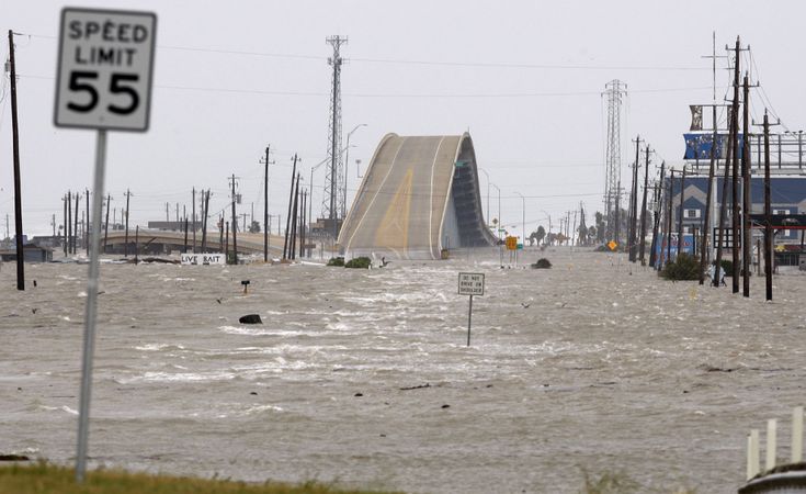 a flooded street with cars and signs in the water near power lines, buildings and telephone poles