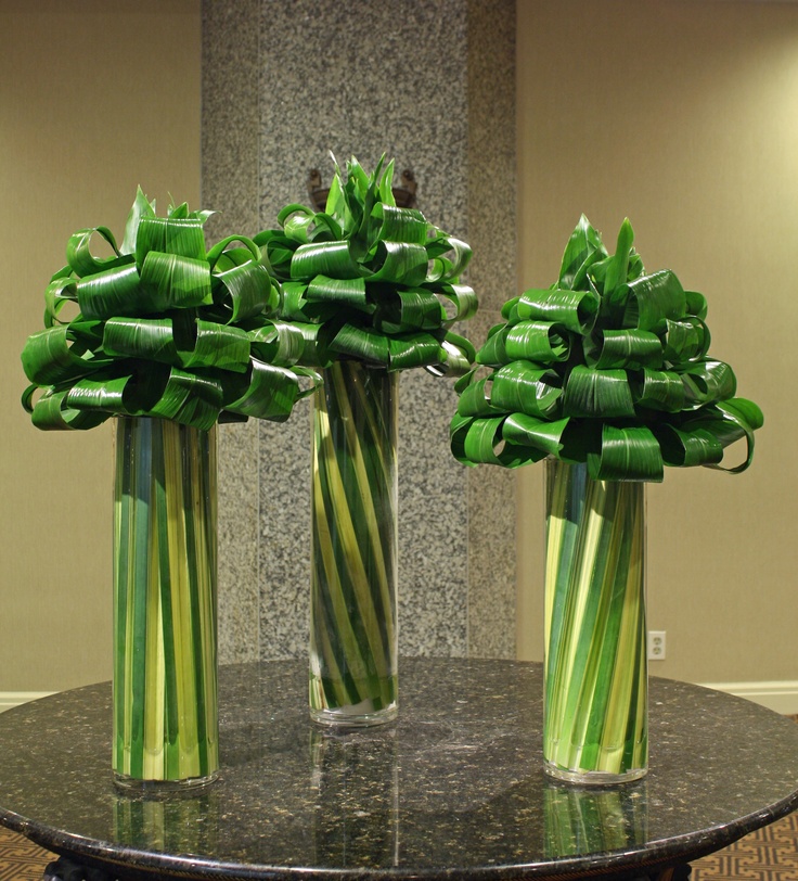 three glass vases with green flowers in them on a black marble table and beige walls