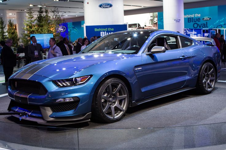 a blue ford mustang car on display at an auto show with people looking around it