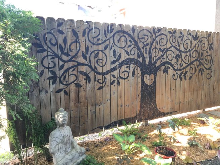 a statue sitting next to a wooden fence with a tree on it's side