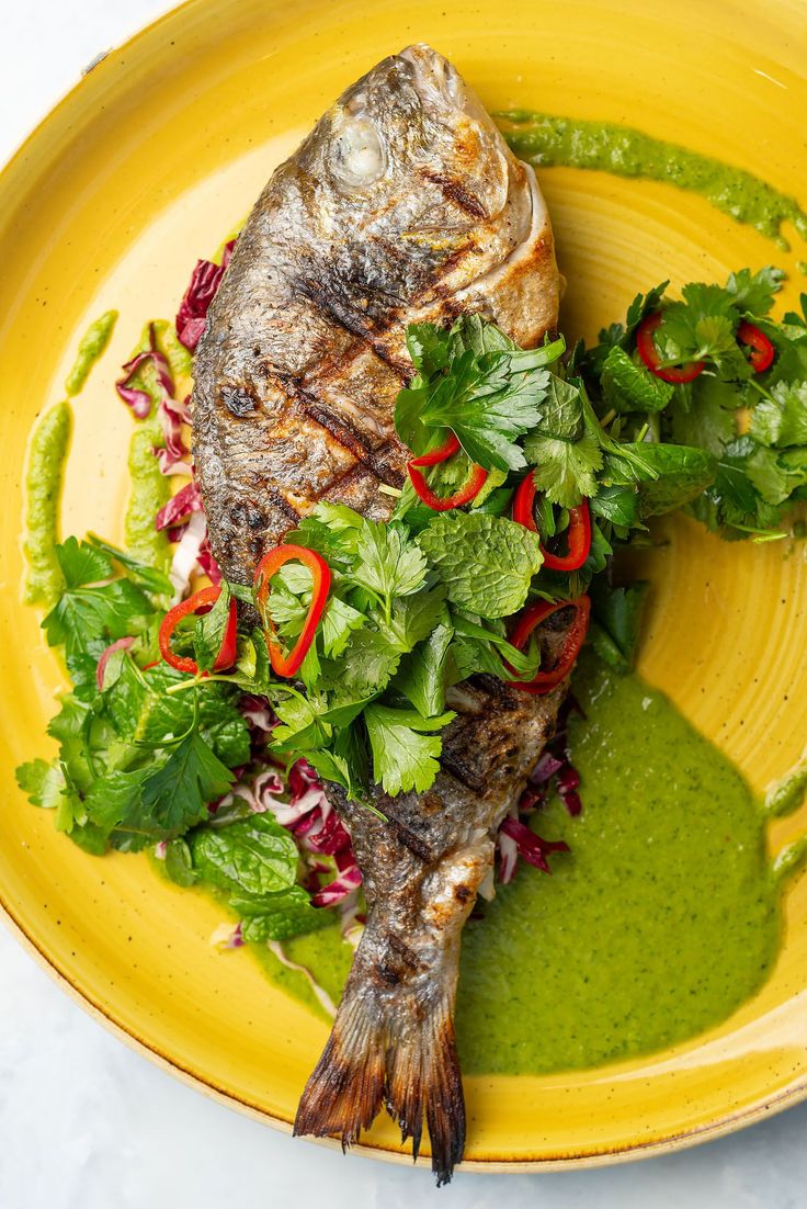 a yellow plate topped with fish covered in green sauce and garnished with cilantro