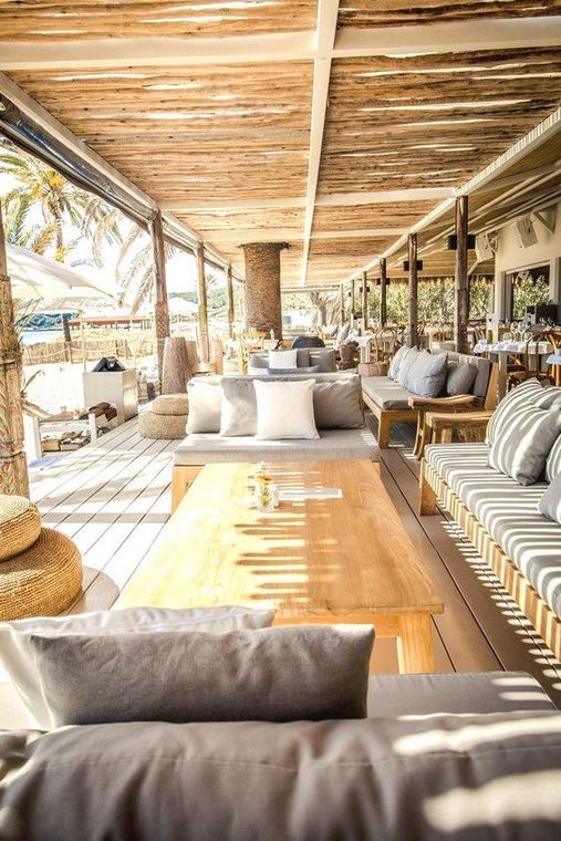 a living room filled with lots of furniture under a wooden roof over looking the ocean