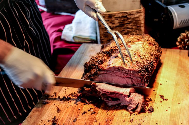 a person cutting up a piece of meat with a knife and fork on a wooden board