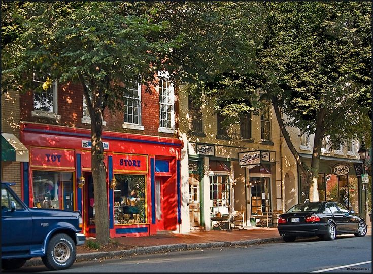 two cars are parked on the street in front of storefronts and trees,